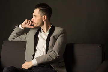 young serious man with an unshaven face in a suit with a pensive face on a dark background