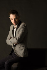 young serious man with an unshaven face in a suit with a pensive face on a dark background