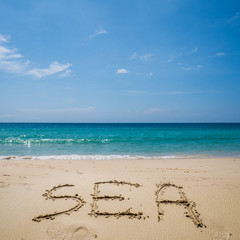 Fototapeta na wymiar Sea written on the beautiful sandy beach over blue sea and sky background