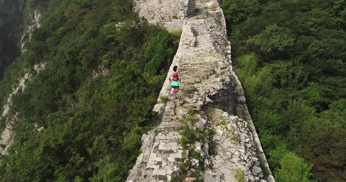 aerial view of young fitness woman trail runner running on top of great wall