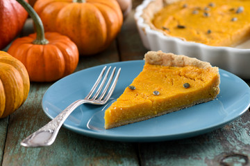 Homemade yummy pumpkin tart with pumpkin seeds on blue plate with decorative pumpkins on background