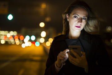 young handsom caucasian woman holding a smartphone on the dark city