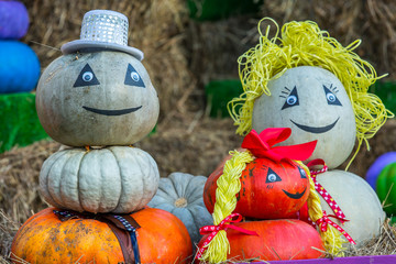 The figure of a family from mom, dad and daughter with braids, assembled from pumpkins, is located in the street around the sheaves of hay. Colorful autumn in Moscow city, Russia.