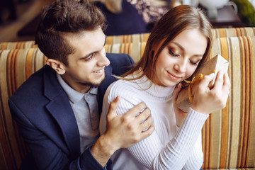 The young man gives a gift to his beloved woman at the coffee shop - the concept of happiness, relationships and celebration