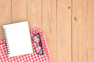 Blank book and eyeglasses on red plaid over wooden of brown, copy space, top view