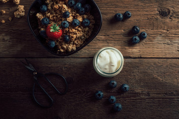 Cereal bowl with fresh fruits on dark old wood table top. Healthy breakfast ingredients with granola, berries and yogurt. Top view.