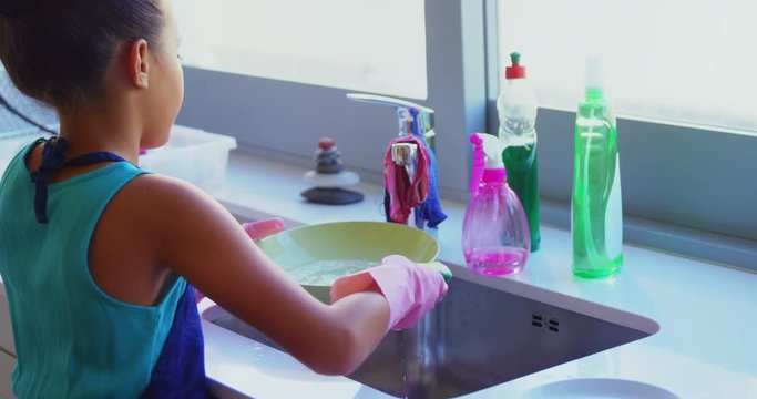 Cute little girl washing plate in kitchen sink 