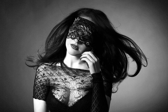 Sexy girl in black lingerie on black background. Erotic photoshoot charming attractive woman with a blindfold mask on her face. The girl's hair flying in the air