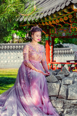 Fototapeta premium Beautiful woman in pink dress is sitting on rock. The background of Japanese architecture in the garden. Spring garden.