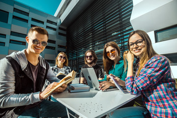 Students wear sunglasses have pleasant break talk on table with laptop and books before modern...