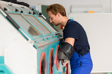 Worker operating a sandblast machine in a metal workshop