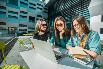 Group of students have study conversation on table with laptop and books before modern building, sunny day