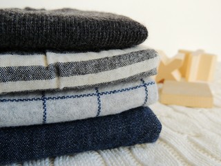 Pile of kids cotton navy gray white clothes on white knitted background. Different texture. Wooden toys.