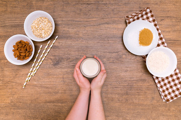 Plant alternative milk recipe: almond, oat, rice in woman hands on the wood background