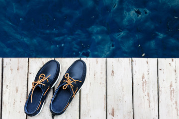 Blue leather men's top sider shoes or boat shoes with white sole on a white wooden pier or on a white wooden boards near the water, or rivers, or lakes, or the sea. Fashion advertising shoes photos.