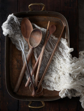 Long wooden spoons nestled in cheesecloth and copper roasting pan
