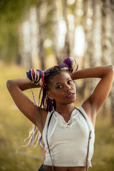 Fototapeta premium portrait of a beautiful young African American girl with a dreddy hairdress on a park background, nature, deciduous forest, photo walk concept in the fresh air
