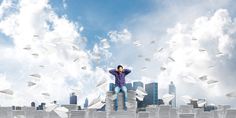 Attractive man sitting on pile of paper documents.