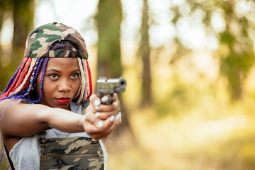 Portrait of a beautiful young African American girl with a dreadna haircut with a gun in her hands. she aims at the attacker. photo self defense concept