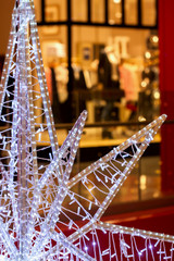 Close-up of piece of large decorative Christmas star on background of bright shop windows. Christmas gifts, shoping concept.