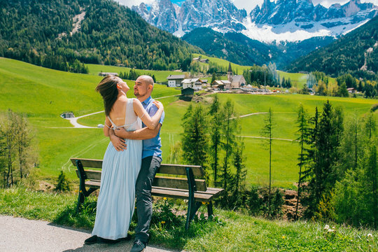 Young couple admires the view in relaxation. Famous best alpine place. Santa Maddalena village with magical Dolomites mountains in background, Val di Funes valley, Trentino Alto Adige Italy