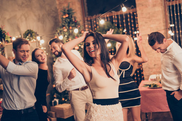 Celebrating newyear. Gorgeous brunette elegant charming lady with raised hands, in beige outfit, group of festive youth on fancy feast, classy outfits, all night, indoors event