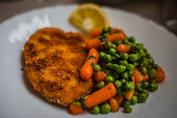Plate of cotoletta with carrots and peas