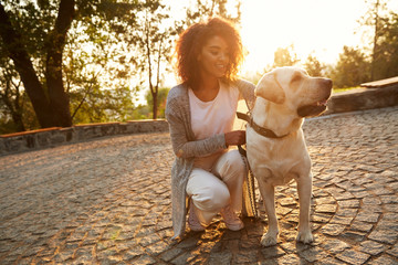 Young smiling lady in casual clothes sitting and hugging dog in park