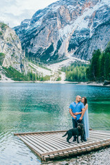 Fototapeta na wymiar Couple with dog. Beautiful young couple playing with dog while sitting near the lake braies in south tyrol, italy