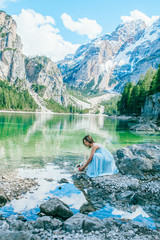 Woman in long blue dress stay on stone near  braies lake in south tyrol, italy. Reflection in the water.