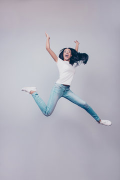 Success, dream, femenine girlish life concept. Chill relaxing mode. Excited mixed race brunette lady model is jumping up, wearing casual clothes, white shoes, on pure light grey background,