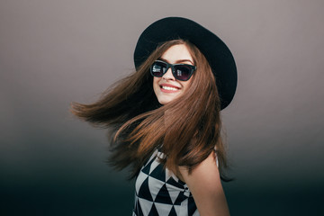 Young beautiful fashionable woman with trendy makeup in black hat and glasses on the grey background . Model looking at camera, wearing stylish eyeglasses. Female fashion, beauty concept.

