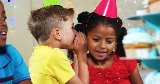 Boy whispering to girl while sitting with friends during birthday party 