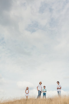 Four kids standing in a golden field against a cloudy summer sky