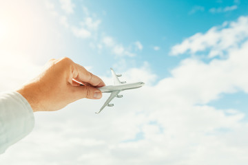 hand holding airplane model in front of cloudy blue sky background. air transportation concept.