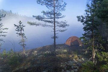 Orange tourist tent against a hazy lake. Karelia, Russia.