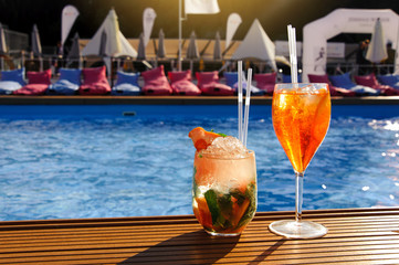 A glass with an orange cocktail near the pool