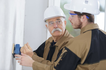 young builder and teacher sanding wall indoors