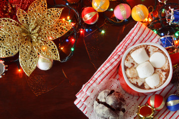 cosy christmas eve pattern: christmas lights, winter hot spicy drink cacao with marshmallows and chocolate cookies on background of striped blanket, electric lights and christmas tree decoration 