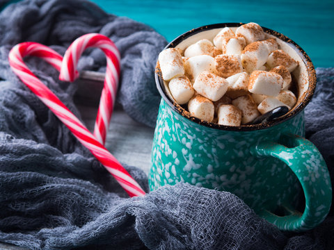 Hot chocolate with marshmallows on green background. Christmas winter still life with red candy canes in heart shape