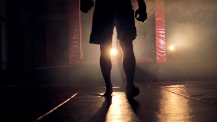 A dark male shape walks away from a fighting cage. 