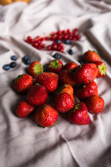 A large guest of juicy red strawberries lies on draped fabric. blueberries, red currants in the...