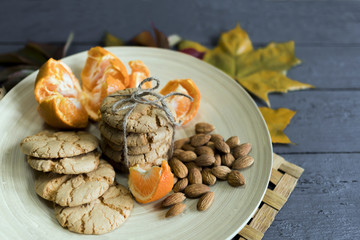 Tasty almond cookies on a wooden plate surrounded by autumn leaves