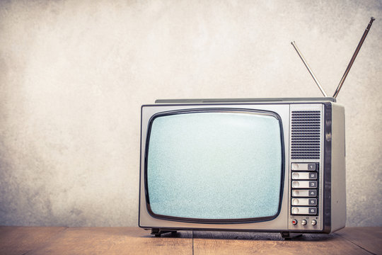 Retro old analog TV set receiver with monochrome static noise on display front textured concrete wall background. Television broadcasting concept. Vintage style filtered photo