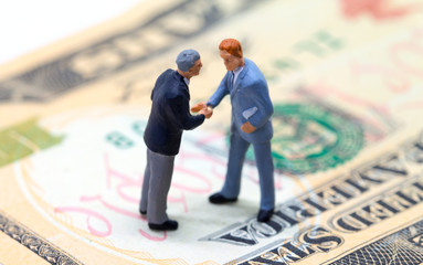 Businessmen shaking hands on american dollar. Tiny businessmen figurines on money background.