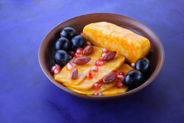 Orange cheese, sliced cheese, a sort of hard cheese, marbled cheese, dark blue grapes, peanuts and pomegranate seeds in a clay plate on a dark blue background in retro style
