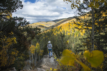Obraz premium a woman standing on a rock overlooking a beautiful mountainside covered in aspen with fall foliage