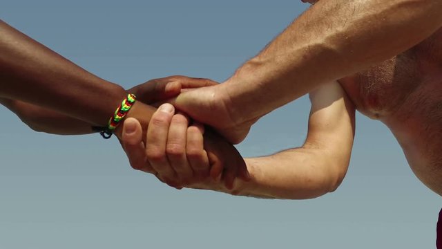 Multicultural people make equality handshake on beach against blue sky