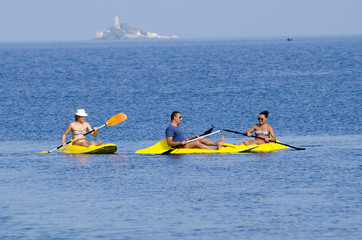 Young people are kayaking on a sea in beautiful nature with island at background. Summer sunny day in outdoor