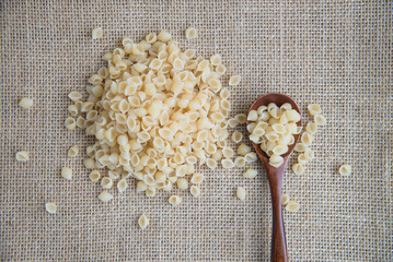Raw pasta in wooden spoon on sack rustic background . Natural and healthy food concept.
